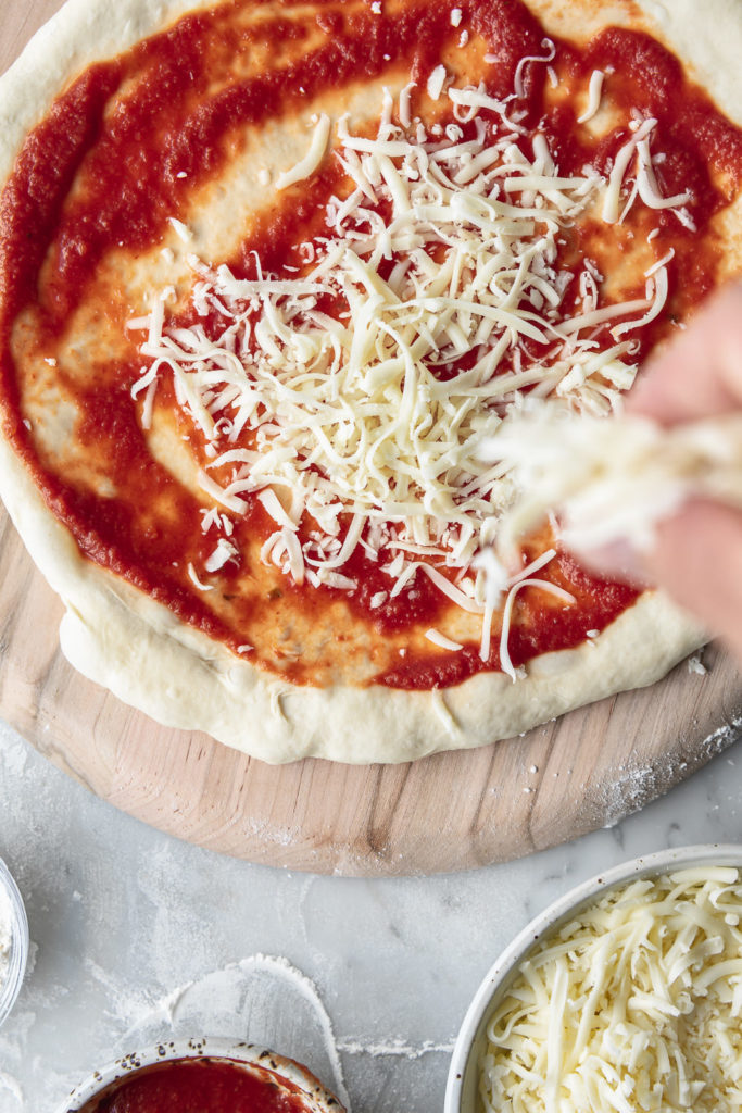 adding cheese to chewy artisan pizza dough